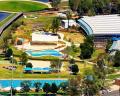 Aerial view of a recreational complex featuring pools, landscaped greenery, and a large building near a lake.