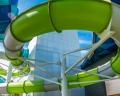 A vibrant green water slide twists and turns against a bright blue sky, surrounded by modern architecture.