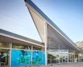 Modern building with a striking angular roof and large glass windows, featuring colorful mural artwork on the façade.