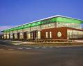 Modern building with large glass windows and a green roof, illuminated at dusk, located at a street corner.