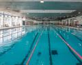 Indoor swimming pool with clear blue water, multiple lanes, and swimmers engaged in various activities along the sides.