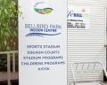 Sign for Bell Street Park Leisure Centre featuring amenities like sports stadium, squash courts, and children's programs, near an entrance.