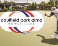 An elderly man bowls on a green lawn at Caulfield Park Alma Bowls Club, with the club's logo prominently displayed.