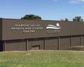 Signage for Diamond Valley Sports and Fitness Centre on a brown building, with green hills in the foreground and trees in the background.