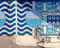 Vibrant blue mural featuring wavy patterns and circular designs, set against a street scene with a parked bicycle.