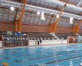 Indoor swimming pool with blue water, high ceilings, and bright lighting; viewing area with benches in the background.