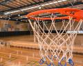 A close-up view of a basketball hoop in a spacious indoor gymnasium with polished wooden floors and bright overhead lights.