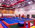 A gym filled with young gymnasts practicing on balance beams at the Imberhorne Hills Leisure Centre, under bright lights.