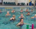 A group of seniors participates in a water aerobics class in a pool, surrounded by colorful water bottles and a supportive atmosphere.