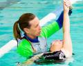 A swimming instructor supports a young swimmer in a pool, helping them practice their skills while ensuring safety and guidance.