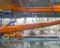 Bright orange water slide curving down into a pool, with blue support structures and a person near the base in a recreational center.