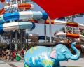 Colorful elephant statue on green grass with vibrant water slides in the background, offering a playful atmosphere at a water park.