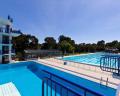 An outdoor swimming pool complex featuring a diving platform, multiple lanes, and surrounded by greenery under a clear blue sky.