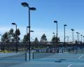 A wide view of a bright blue tennis court complex with multiple courts and tall lights under a clear blue sky.