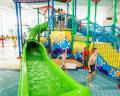 Children playing at a colorful indoor water slide complex with stairs, vibrant artwork, and a green slide.