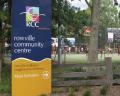 Rowville Community Centre sign in front of a lively recreation area with people engaging in outdoor sports and activities.