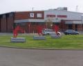 Exterior of a sports training facility featuring three red athlete sculptures on a grassy area with cars parked nearby.