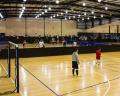 A spacious indoor sports facility with players engaged in a match on a wooden court, surrounded by spectators in the stands.