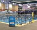 Indoor swimming pool with lane markers, a safety sign, and large windows allowing natural light in.