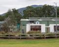 Modern building with a green exterior, surrounded by landscaped gardens and mountains in the background under a cloudy sky.