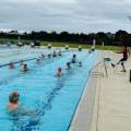 An indoor inground level swimming pool with multiple lanes divided by ropes and a group of swimmers doing water aerobics.