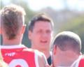 Three individuals are engaged in discussion on a sunny day, wearing red sports jerseys with visible team logos.