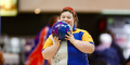 Photo of a person holding a blue bowling ball, wearing a yellow and blue shirt