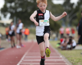 A young athlete in a black and white uniform leaps forward on a track, showcasing determination and athleticism during a sporting event.