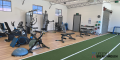 Modern gym interior featuring exercise equipment, weights, and a green turf area, designed for fitness training and workouts.