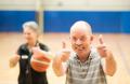 Two individuals in a gym, one holding a basketball, both giving thumbs-up in a lively atmosphere.