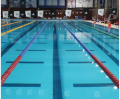 A swimming pool featuring multiple lanes marked with colorful ropes and reflections, indoors with banners displayed on the walls.