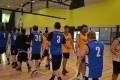 A group of basketball players in blue and yellow jerseys shake hands after a game inside a gym with a bright yellow wall.