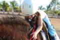 A small girl is happily petting a horse, enjoying a warm day in a peaceful outdoor scene