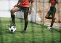 Two soccer players in red uniforms on a green field; one rests a foot on a soccer ball while the other stands nearby.