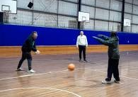 Two players are actively passing a basketball in a gymnasium, while a third person watches nearby.